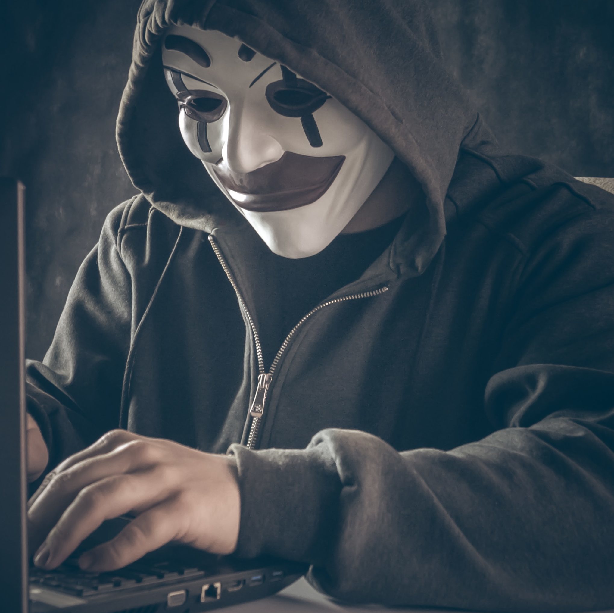 Hacker with a hoodie typing on a laptop