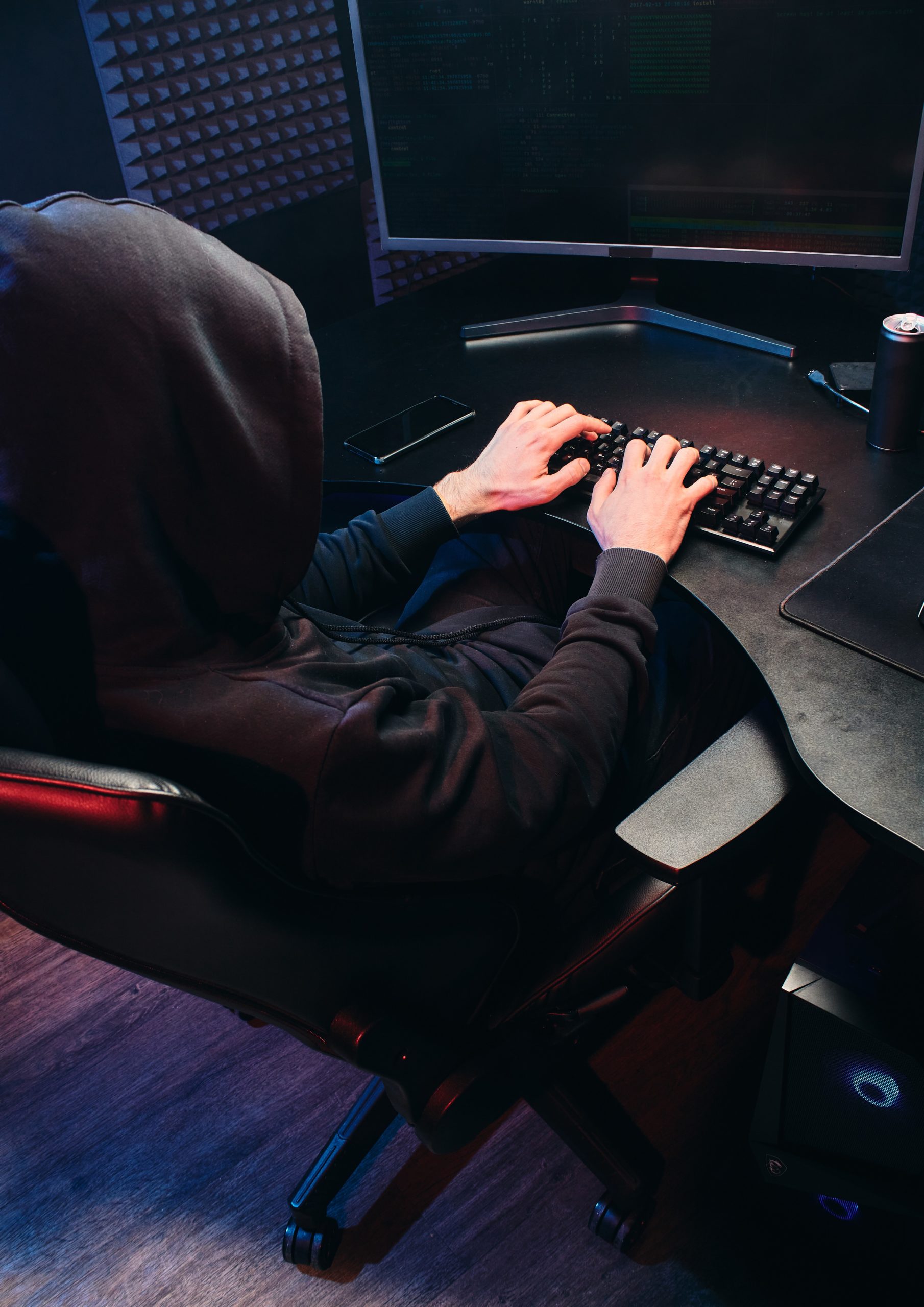 Hacker wearing a black hoodie typing on a computer
